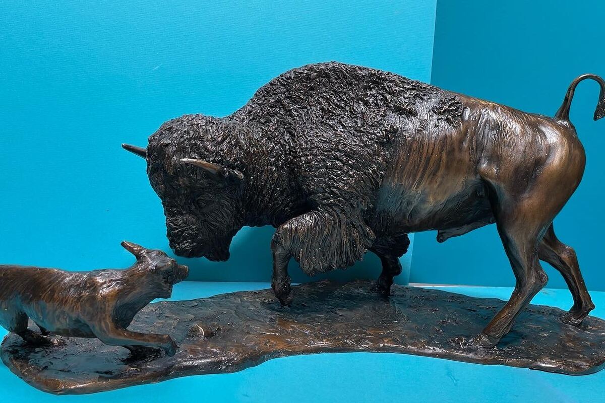 Bronze bison with its calf facing a coyote across a sculpted base