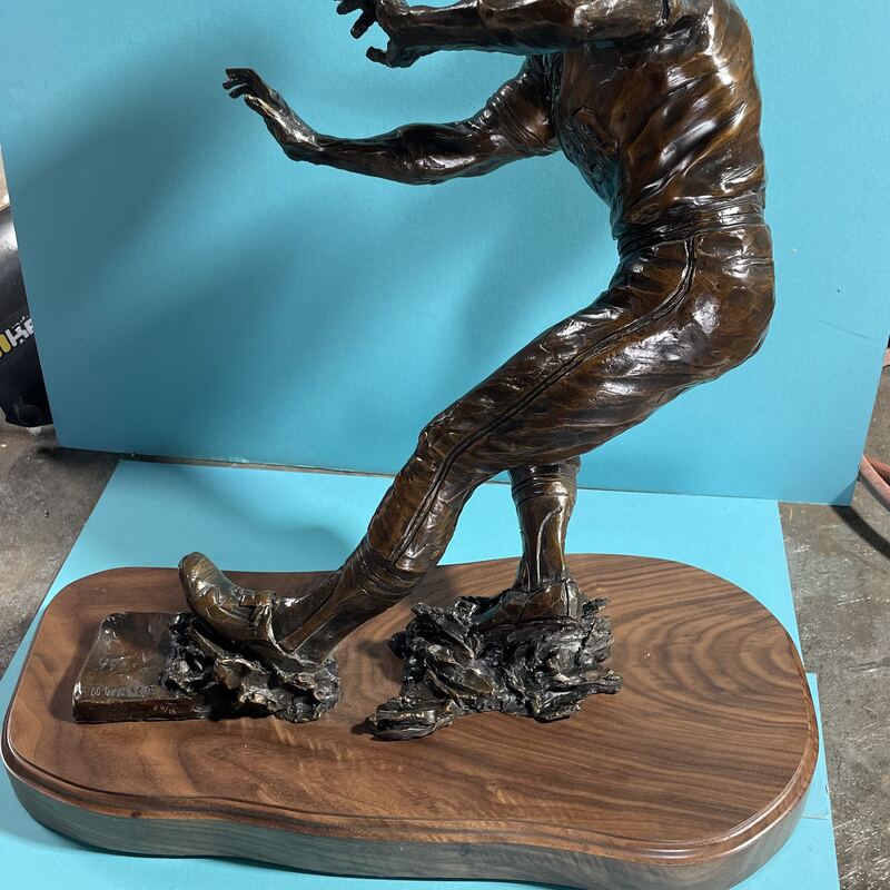 Bronze of a boy in a cap bracing himself, mounted on a walnut base