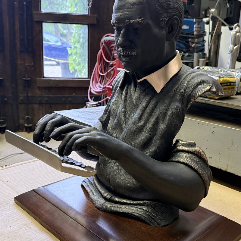 Bronze half-figure of a man typing, on a wooden plinth