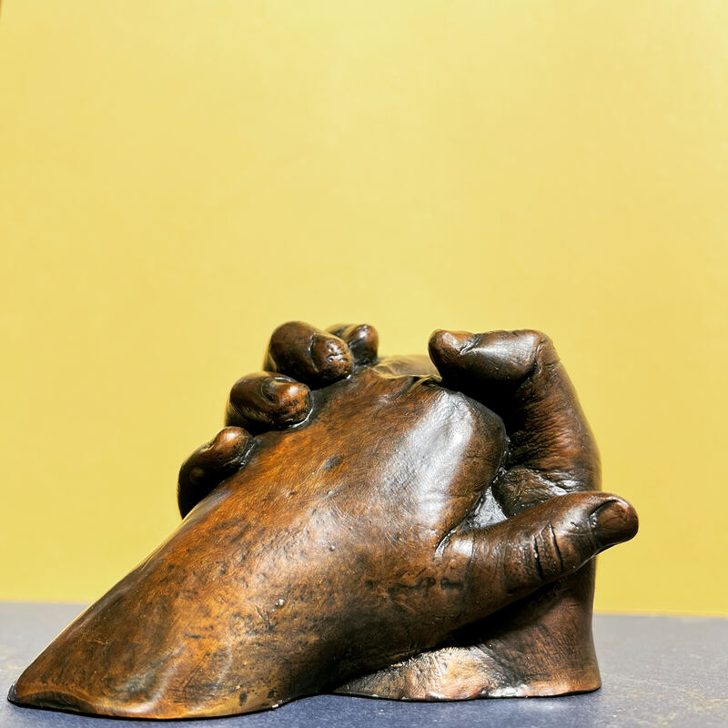 Cast bronze of two clasped hands with a warm polished patina