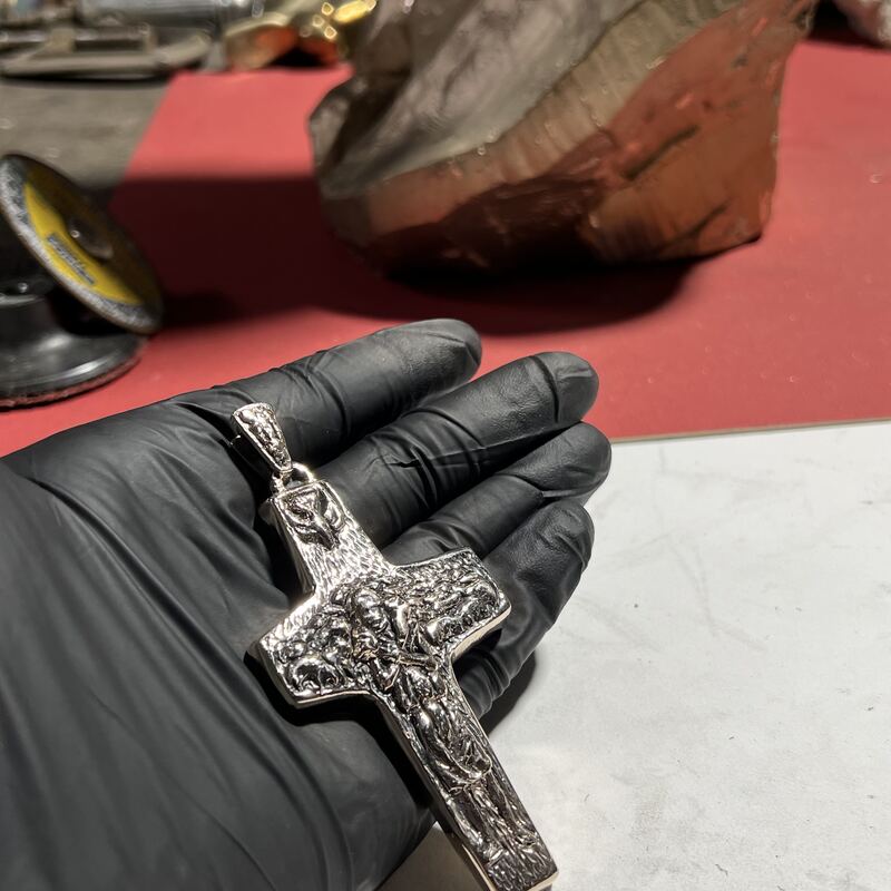 Cast bronze crucifix pendant held in a gloved hand