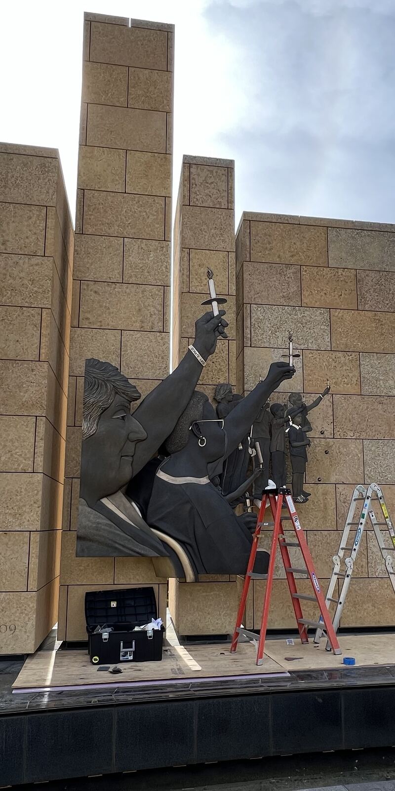 Bronze relief being installed on a stone monument, ladders at its base