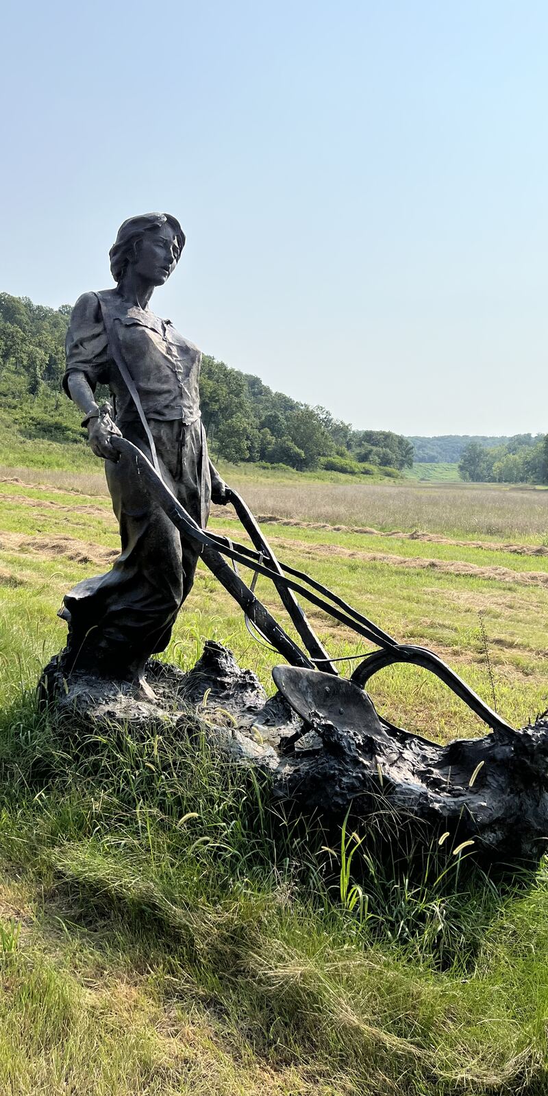 Bronze farmer and plow set in a field below wooded hills