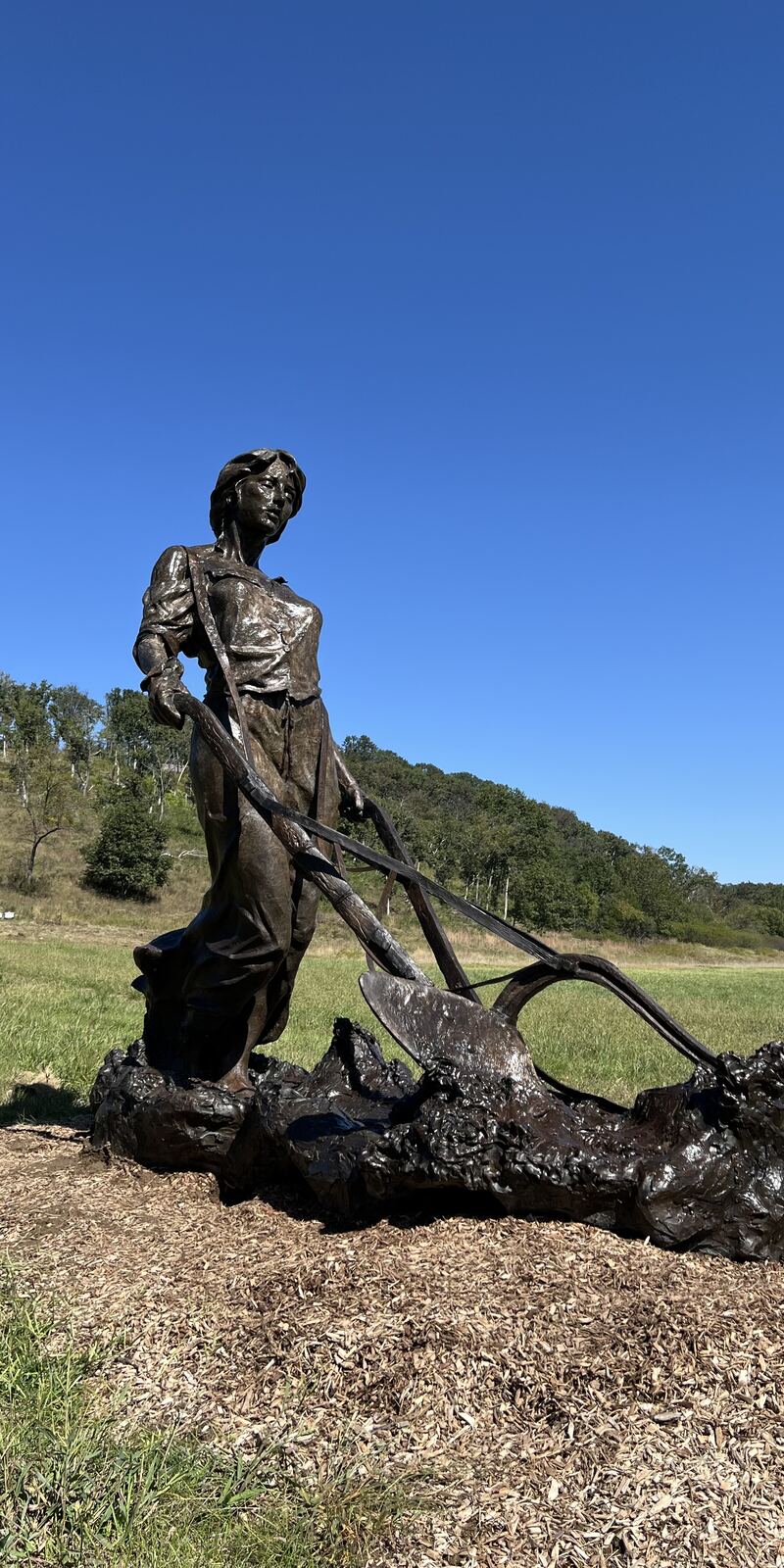 Life-size bronze of a farmer behind a horse-drawn plow, installed on a hillside