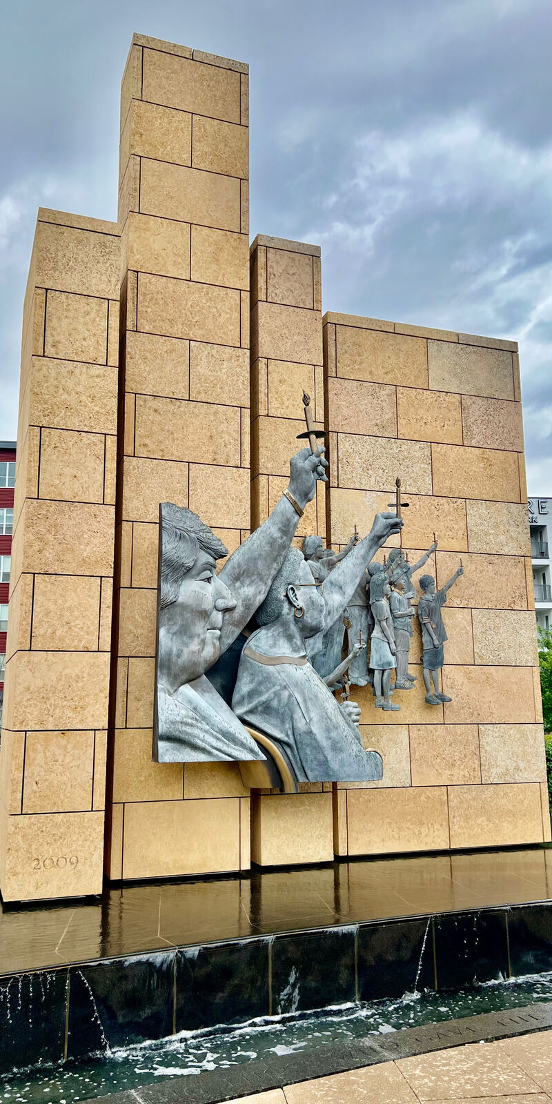 Tall stone monument wall with a bronze figurative relief set into its face